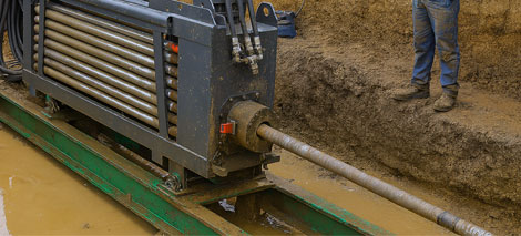 Directional boring machinery in a trench, showcasing equipment for underground pipe installations, with a worker in safety gear nearby.