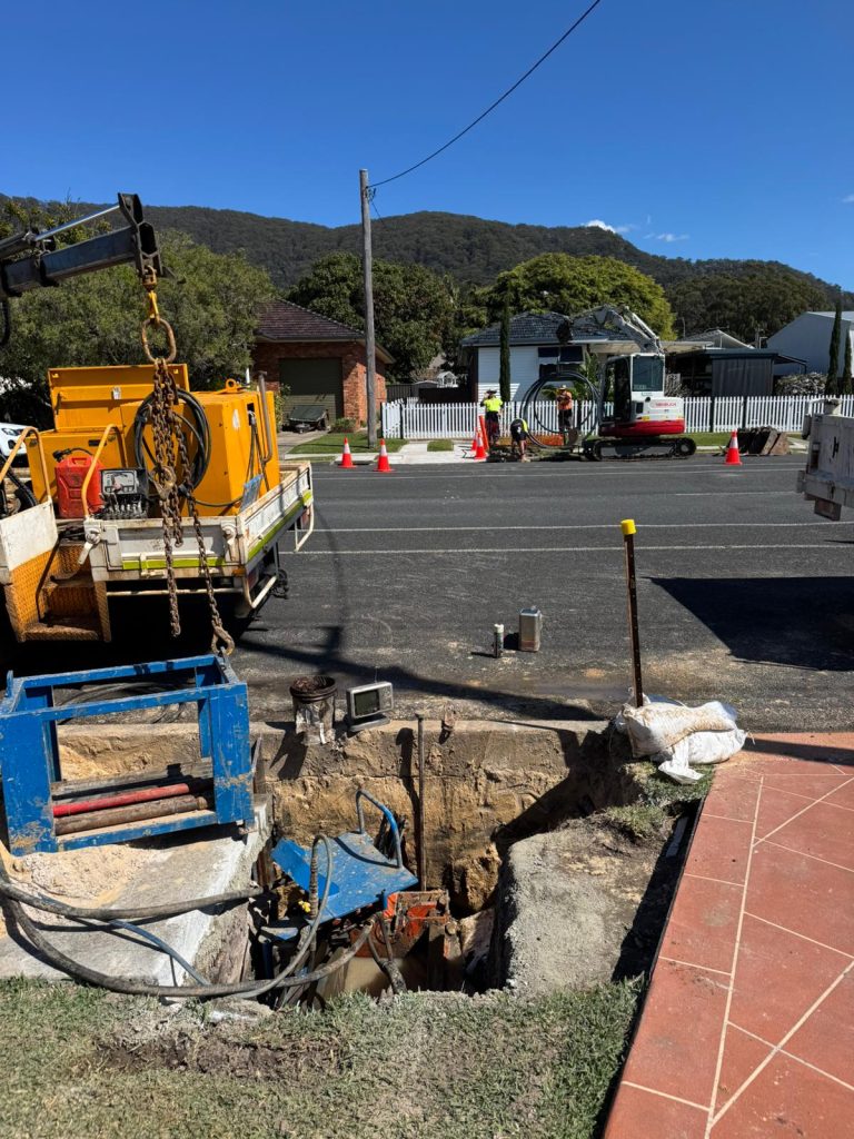 Construction site with trench for horizontal bed boring, featuring a mini-directional boring rig, safety cones, and utility vehicles in a suburban area.