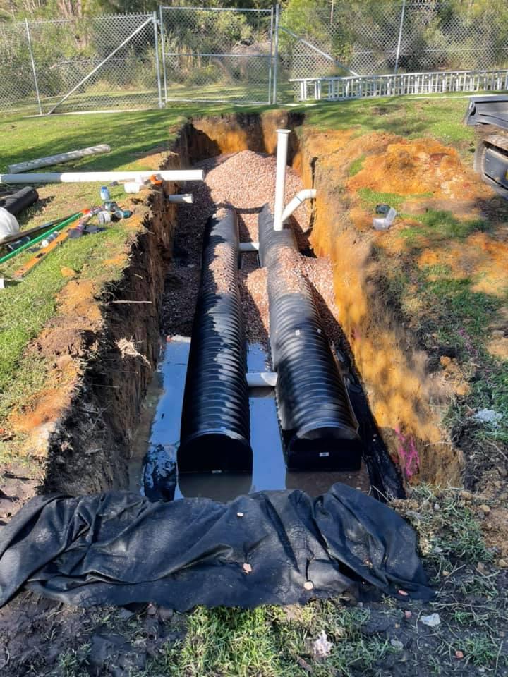 Excavated trench with black drainage pipes and gravel, illustrating plumbing infrastructure installation relevant to emergency plumbing services.
